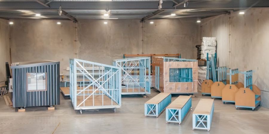 A clad light-gauge steel cabin standing beside the steel frames and floor cassettes it was built from, on Atlas Frames' production floor