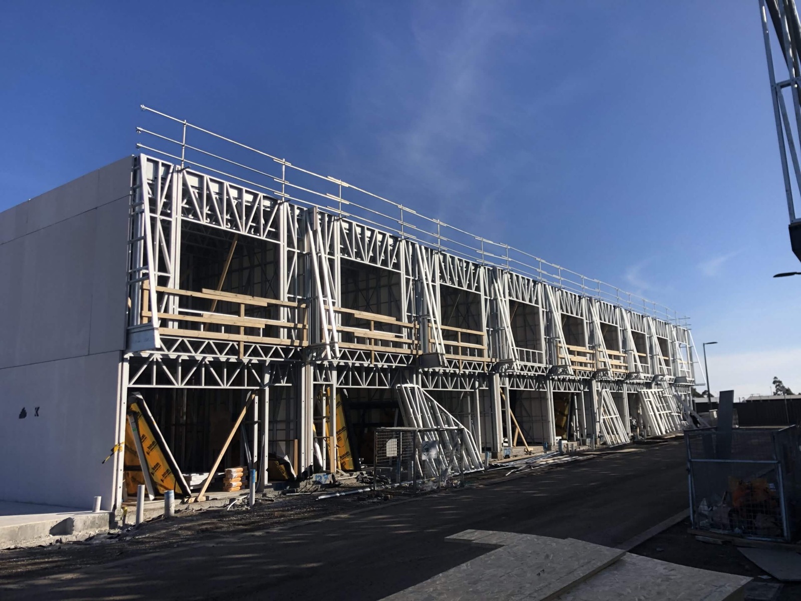 A multi-bay light-gauge steel structure standing under scaffolding on site, framed by Steel Frames Direct
